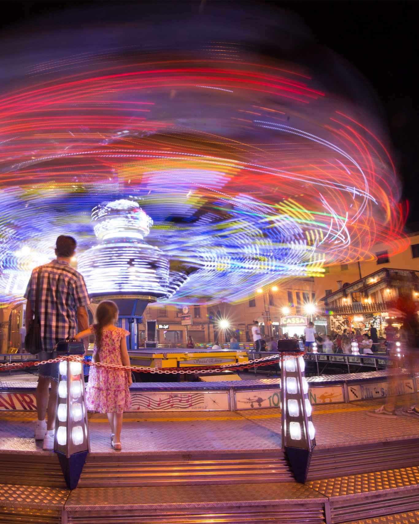 Giostra in movimento fotografata a lunga esposizione di notte, con visitatori in primo piano